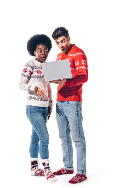Sorprendido pareja multicultural en suéteres usando ordenador portátil, aislado en blanco - foto de stock