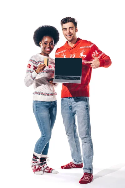 Multikulturelles Paar hält Kreditkarte in der Hand und zeigt auf Laptop mit leerem Bildschirm, isoliert auf weiß — Stockfoto