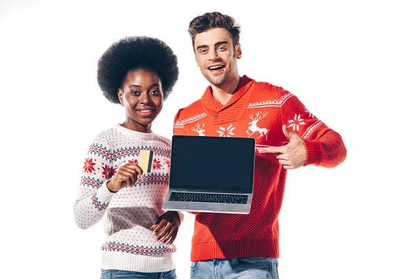 Feliz casal interracial segurando cartão de crédito e apontando para laptop com tela em branco, isolado no branco — Fotografia de Stock
