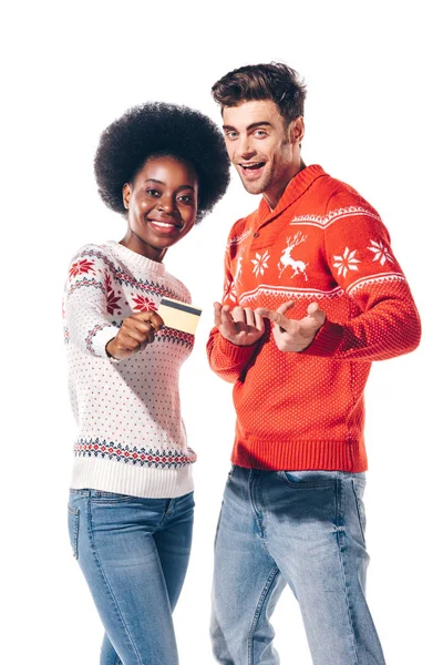 Happy multicultural couple in winter sweaters holding credit card, isolated on white — Stock Photo