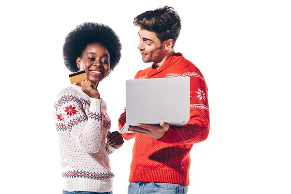 Sonriente pareja interracial usando portátil con tarjeta de crédito, aislado en blanco - foto de stock