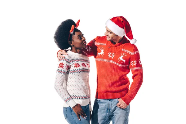 Lächelndes gemischtrassiges Paar mit Weihnachtsmütze und weihnachtlichen Hirschhörnern, isoliert auf weißem Grund — Stockfoto