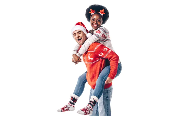 Feliz casal interracial em santa chapéu e Natal chifres piggybacking, isolado no branco — Fotografia de Stock