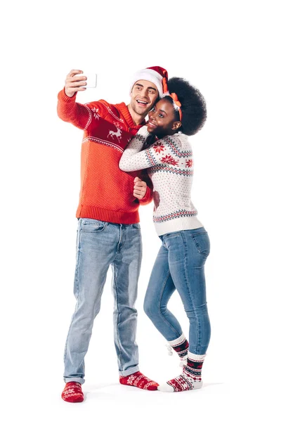 Beautiful interracial couple in santa hat and deer horns taking selfie on smartphone, isolated on white — Stock Photo