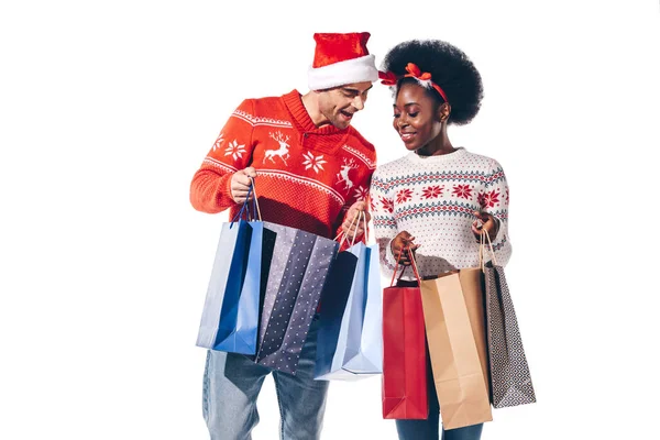 Happy interracial couple in santa hat and deer horns holding shopping bags, isolated on white — Stock Photo