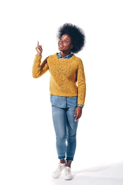 Smiling african american girl in yellow sweater pointing up, isolated on white — Stock Photo