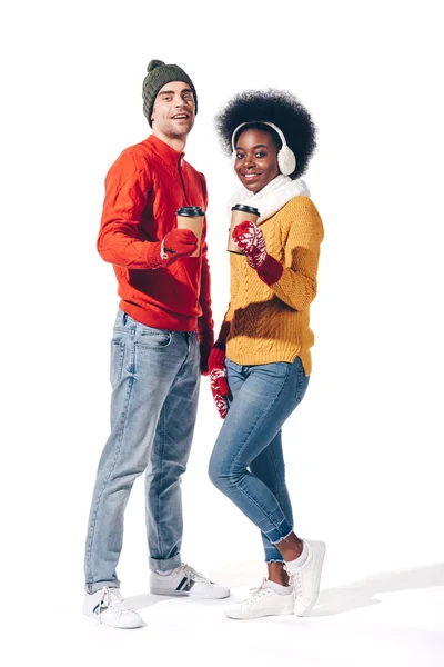 Hermosa joven pareja interracial en ropa de invierno sosteniendo café para llevar, aislado en blanco - foto de stock