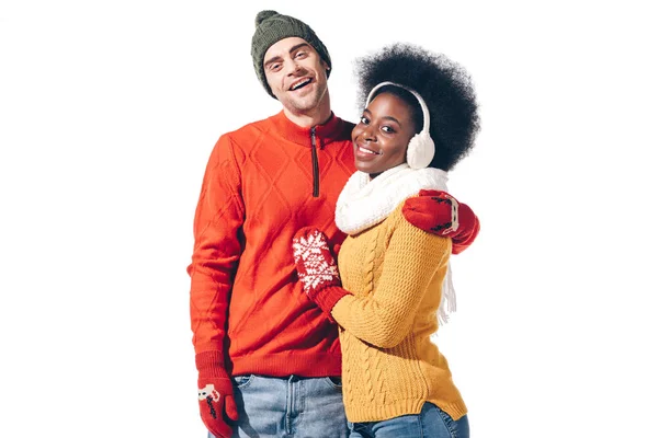 Багатонаціональна пара обіймається светрами і рукавичками, ізольована на білому — стокове фото