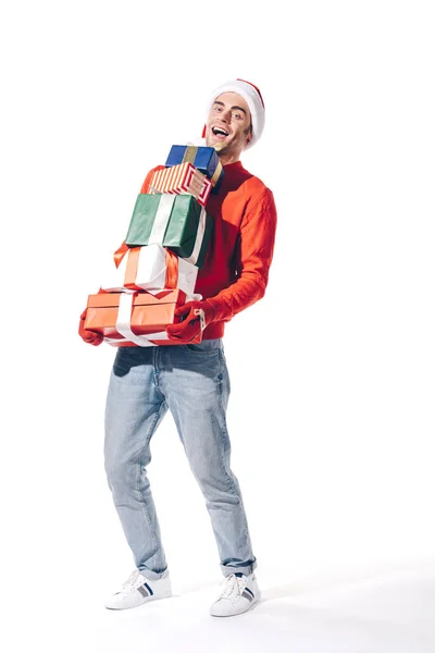 Щасливий чоловік у капелюсі Санта тримає купу різдвяних подарунків, ізольований на білому — стокове фото