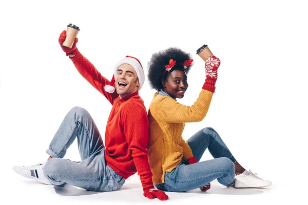 Sorridente coppia multietnica in cappello di Babbo Natale e corna di cervo in possesso di caffè per andare, isolato su bianco — Foto stock