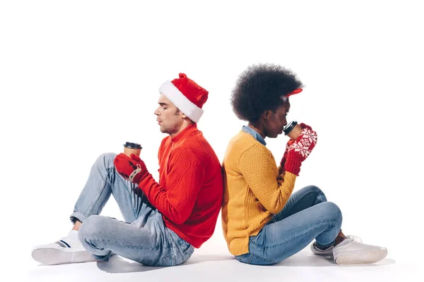 Feliz pareja interracial en sombrero de santa y cuernos de ciervo sosteniendo café para llevar, aislado en blanco - foto de stock