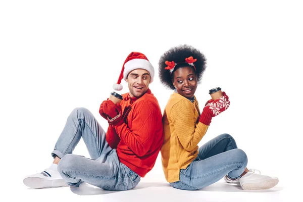 Happy interracial couple in santa hat and deer horns holding coffee to go, isolated on white — Stock Photo