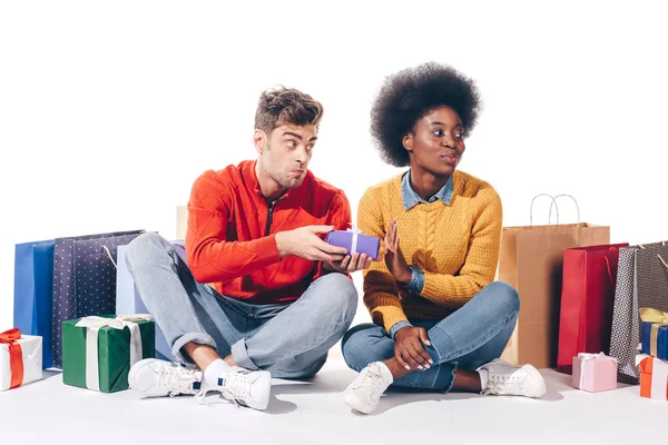 Feliz pareja multiétnica con bolsas de compras y regalos, aislado en blanco - foto de stock