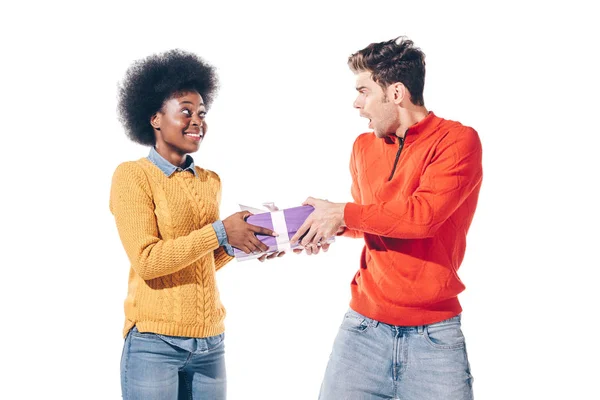 Шокований чоловік і усміхнена афроамериканська дівчина тримає подарунок, ізольовані на білому — стокове фото