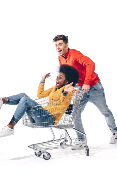 Casal multiétnico se divertindo com carrinho de compras, isolado em branco — Fotografia de Stock