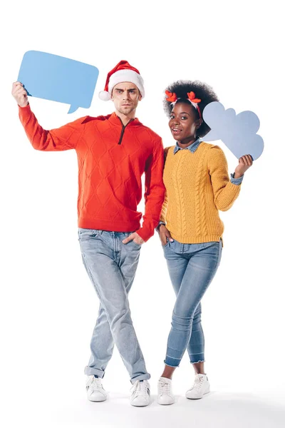 Pareja interracial en sombrero de santa y cuernos de ciervo sosteniendo la burbuja del pensamiento y la burbuja del habla, aislado en blanco - foto de stock