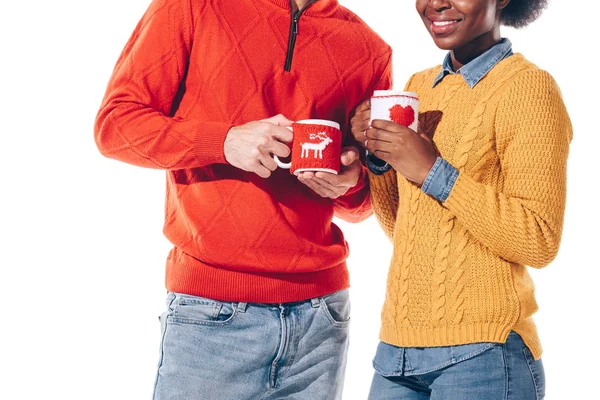 Vue recadrée d'heureux couple multiethnique en chapeau de Père Noël et cornes de cerf buvant du café, isolé sur blanc — Photo de stock