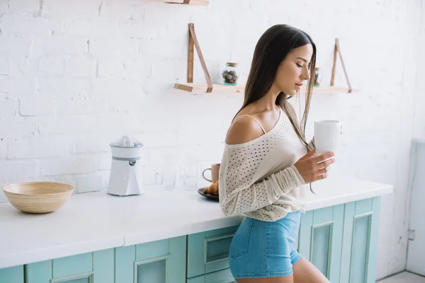 Atractiva mujer sosteniendo la taza de café en la acogedora cocina - foto de stock