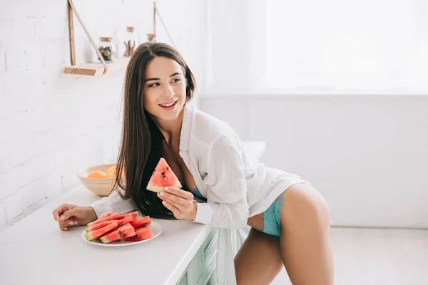 Menina bonita em lingerie e camisa branca comendo melancia na cozinha — Fotografia de Stock