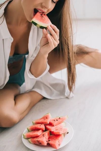 Vue recadrée de femme sensuelle en lingerie et chemise blanche mangeant pastèque sur le sol dans la cuisine — Photo de stock