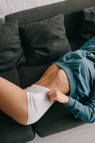 Vista cortada de jovem mulher magra em calcinha branca deitada no sofá — Fotografia de Stock