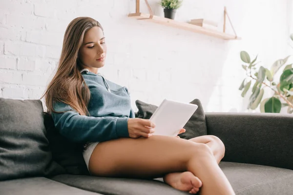 Attractive girl with long hair in panties using digital tablet on sofa — Stock Photo