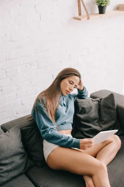 Hermosa mujer en bragas usando tableta digital en sofá gris - foto de stock