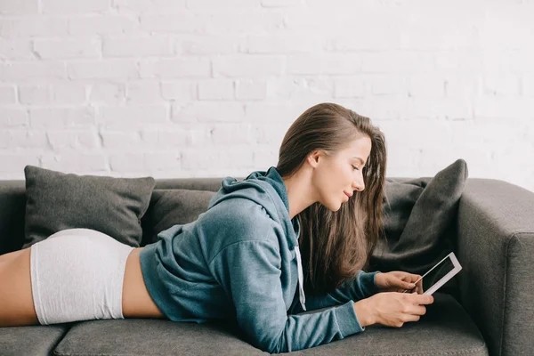 Красива жінка в трусиках, використовуючи цифровий планшет, лежачи на дивані — стокове фото