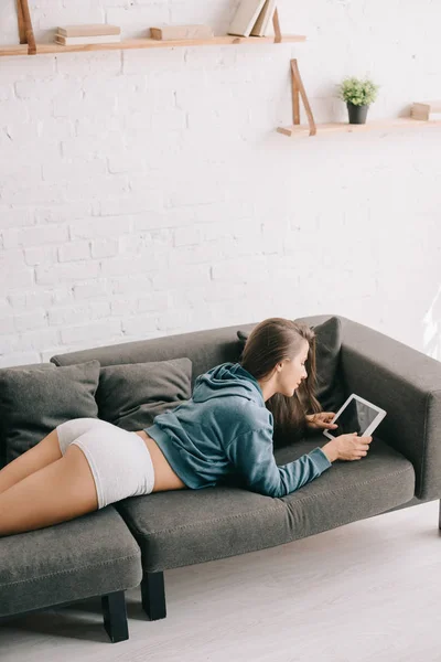 Femme attrayante en culotte en utilisant une tablette numérique tout en étant couché sur le canapé — Photo de stock