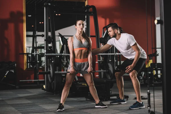 Beau entraîneur soutenant attrayant sportif haltère de levage — Photo de stock