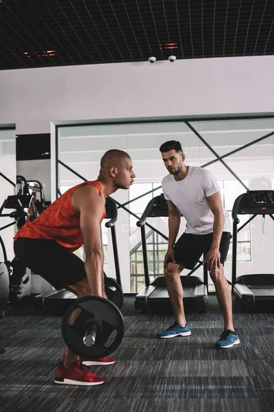 Treinador atencioso instruindo afro-americano desportista levantar barbell — Fotografia de Stock