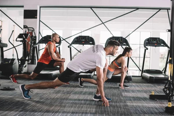 Bonito treinador fazendo lunges exercício em conjunto com atletas multiculturais — Fotografia de Stock