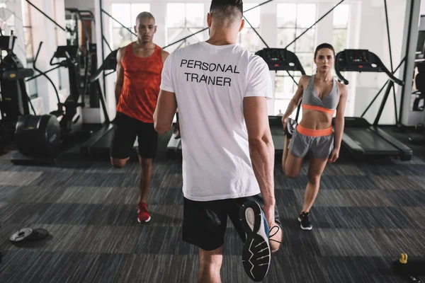 Back view of personal trainer supervising multicultural athletes warming up in gym — Stock Photo