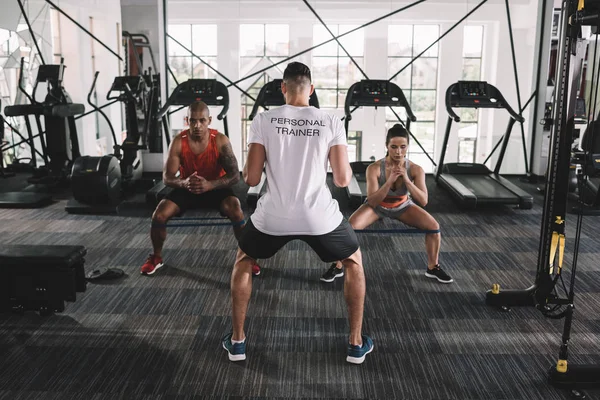 Back view of personal trainer supervising multicultural athletes warming up in gym — Stock Photo