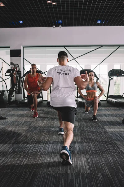 Back view of personal trainer doing lunges exercise together with multicultural athletes — Stock Photo