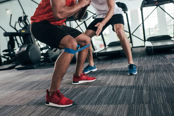 Cropped view of trainer standing near african american sportsman exercising with resistance band — Stock Photo