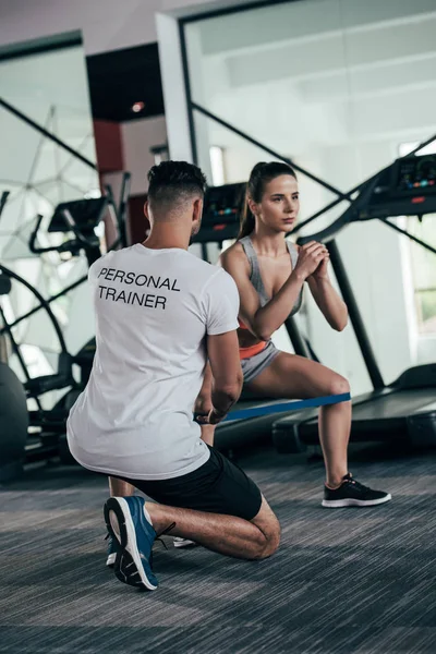 Visão traseira do personal trainer controlando atraente esportista exercitando com banda de resistência — Fotografia de Stock