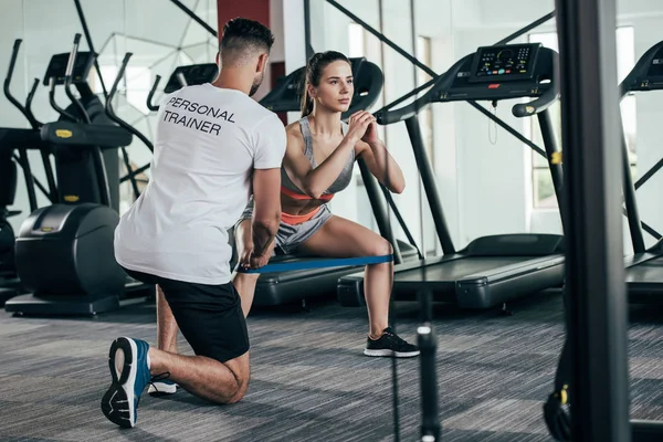 Visão traseira do personal trainer supervisionando jovem esportista exercitando com banda de resistência — Fotografia de Stock