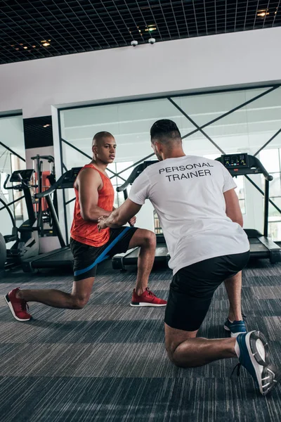 Visão traseira do personal trainer instruindo esportista afro-americano exercitando com expansor — Fotografia de Stock