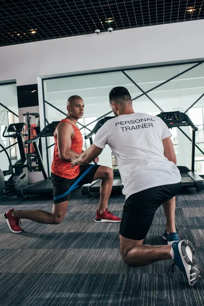 Vue arrière de l'entraîneur personnel instruisant sportif afro-américain exercice avec extenseur — Photo de stock