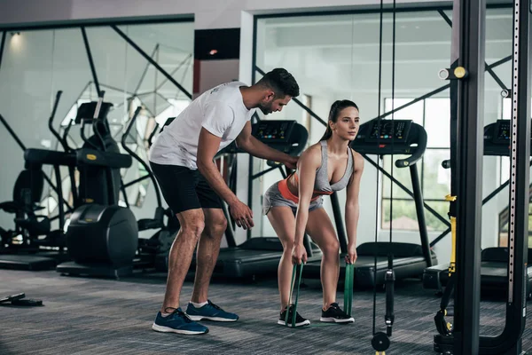 Young trainer supporting athletic sportswoman exercising with resistance bands — Stock Photo