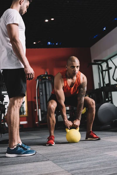 Young trainer supervising african american sportsman lifting weight — Stock Photo