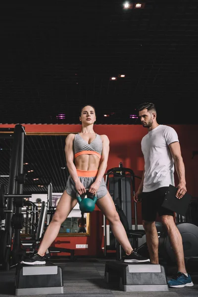 Entrenador atento supervisar joven deportista levantamiento de peso en el gimnasio - foto de stock