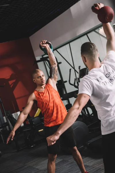 Back view of personal trainer lifting weight together with african american athlele — Stock Photo