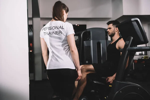 Back view of personal trainer instructing handsome sportsman working out on recumbent elliptical trainer — Stock Photo