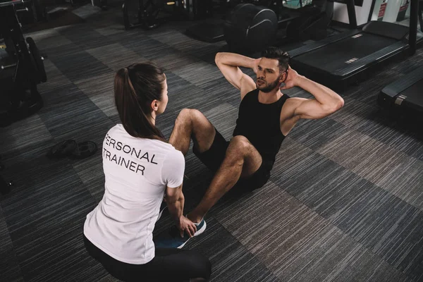 Young trainer supporting handsome sportsman doing push ups — Stock Photo