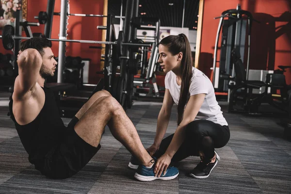 Treinador atraente apoiando desportista bonito fazendo flexões — Fotografia de Stock