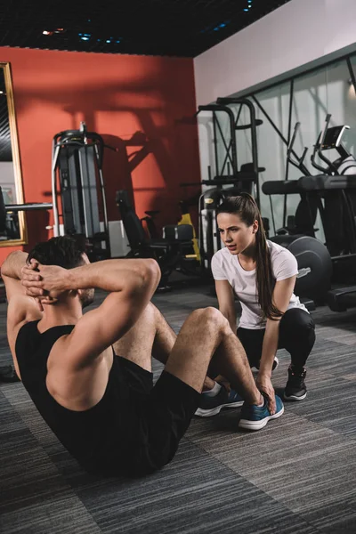 Attractive trainer supporting handsome sportsman doing push ups — Stock Photo