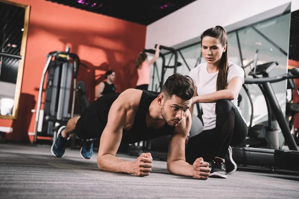 Attraktiver Trainer, der Sportler beim Plankentraining überwacht — Stockfoto