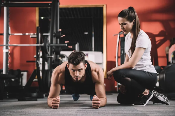 Attentive trainer supervising handsome sportsman doing plank exercise — Stock Photo